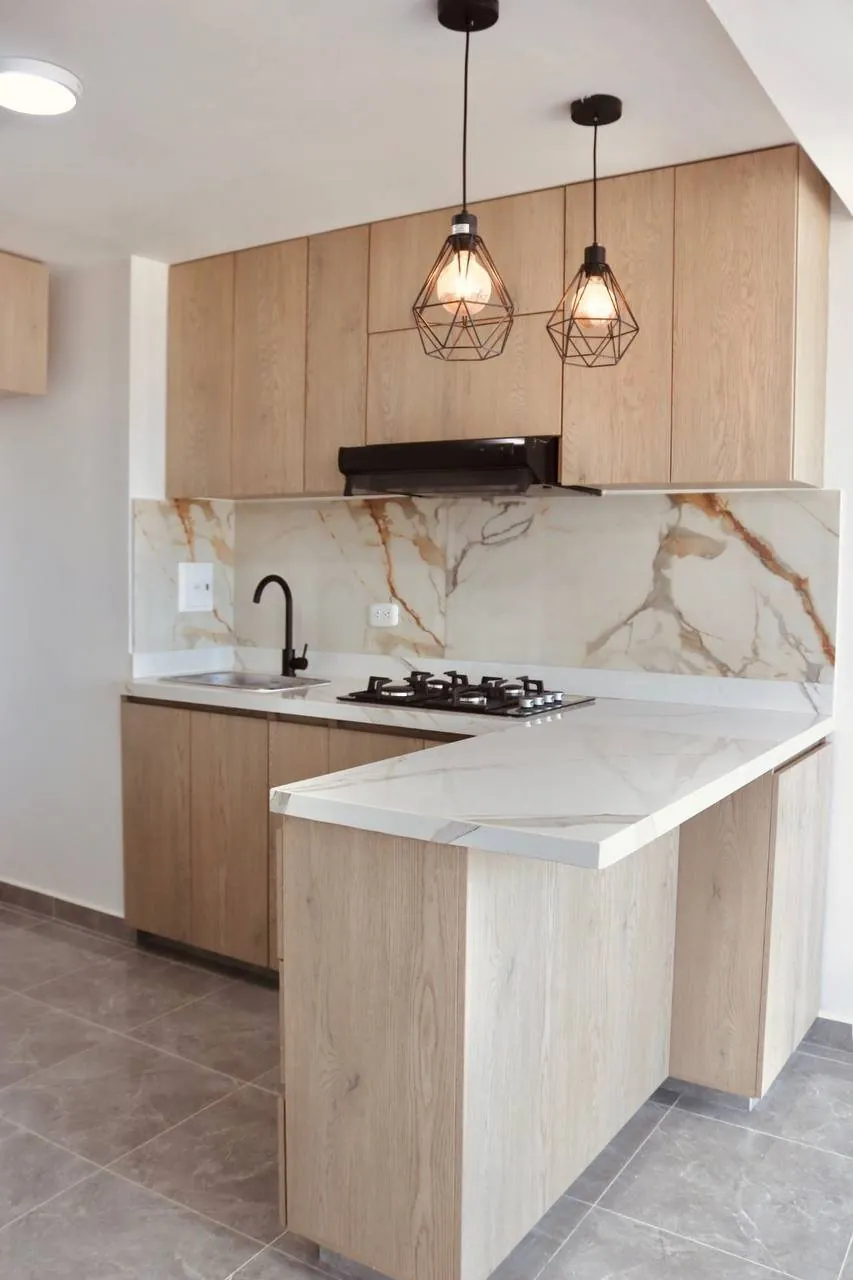 Cocina remodelada con barra en L, muebles en madera clara y lámparas colgantes